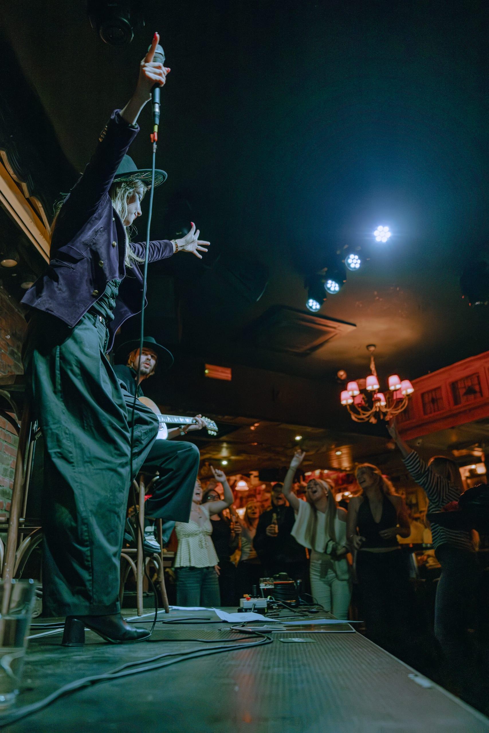 Performer on stage under green light, crowd reaching upward